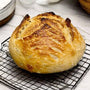 A freshly baked artisan sourdough loaf with a dark mahogany crust and intricate scoring resting on a wire cooling rack.