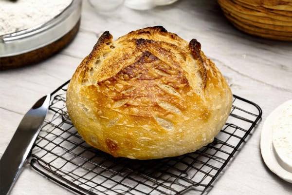 A freshly baked artisan sourdough loaf with a dark mahogany crust and intricate scoring resting on a wire cooling rack.