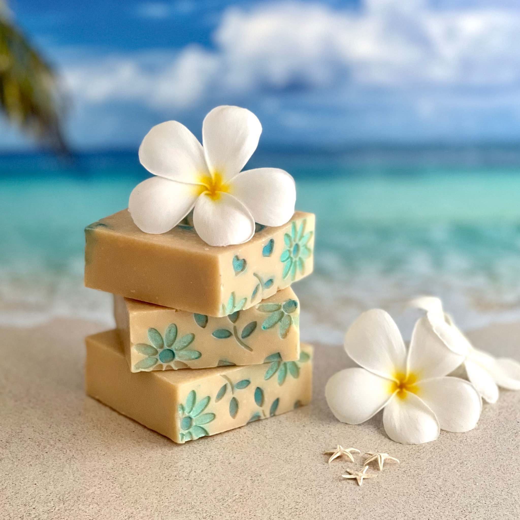 Stack of 3 beautiful On Island Thyme Coconut Milk Soap with floral impressions on a beach with mini-star fish and Plumeria blooms on a beach