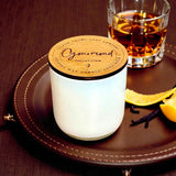Candle burning on a wooden surface with cinnamon sticks and a glass of liquid in the background