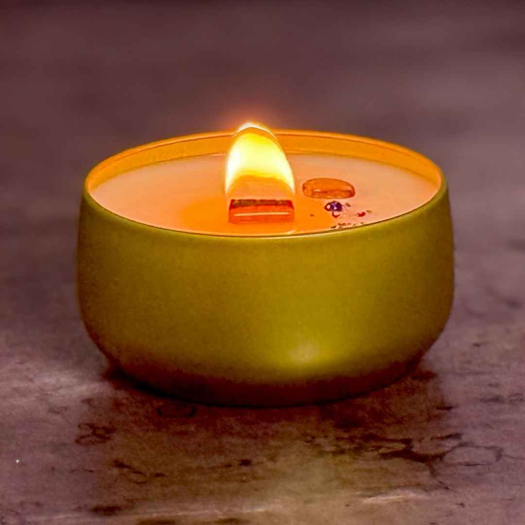 Gold tin candle with a lit wick on a textured surface