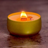 Gold tin candle with a lit wick on a textured surface