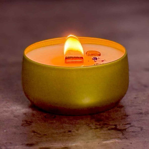 Gold tin candle with a lit wick on a textured surface