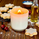 Candle in a glass holder with star-shaped cookies and a bottle of oil on a wooden surface.