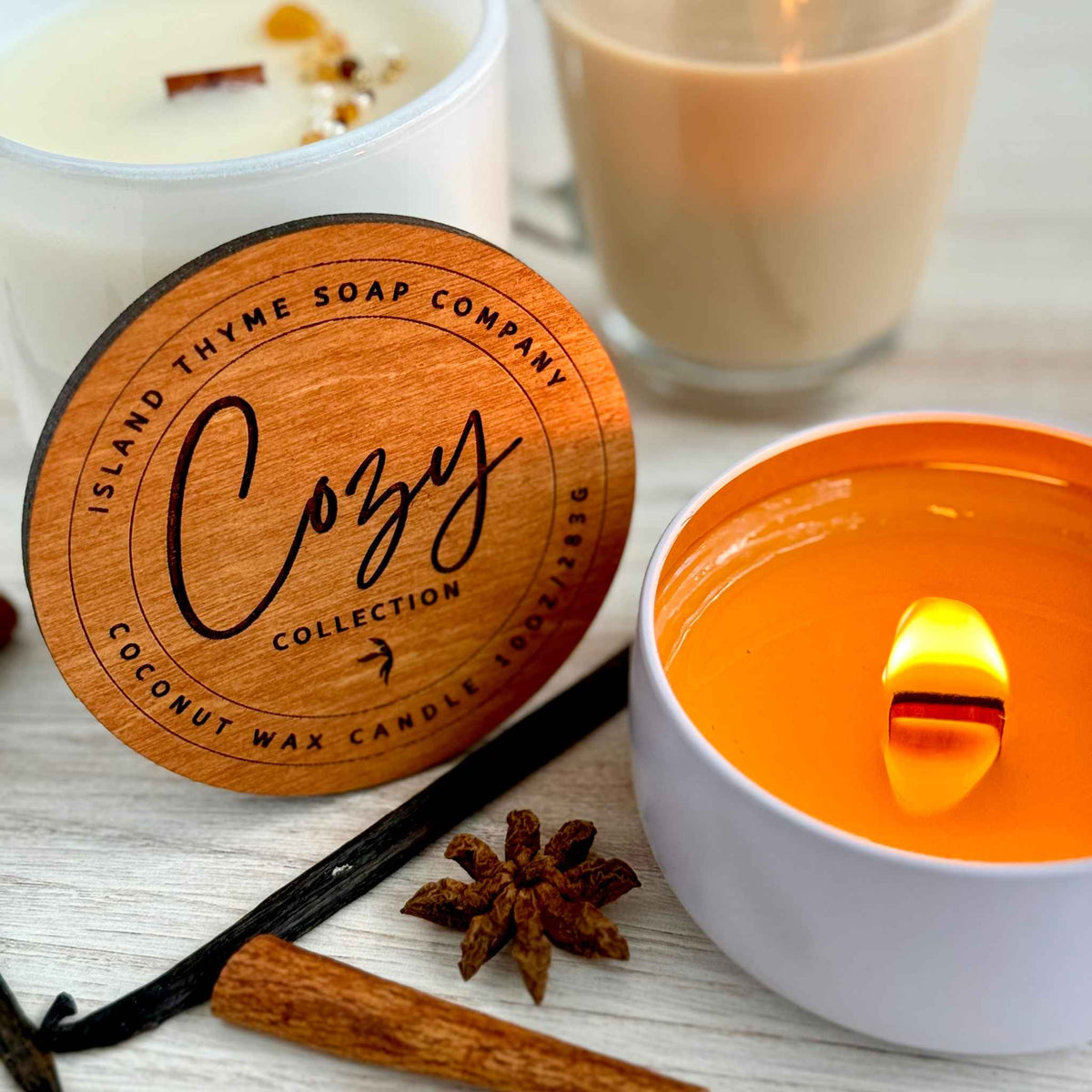 Lit and unlit white coconut wax candles with wood wicks, adorned with amber and brown glass beads. A Chai Latte, cinnamon stick, vanilla bean, and star anise accent the scene.