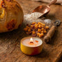 A cozy kitchen counter scene featuring a burning yellow candle tin next to a freshly baked cheddar bacon sourdough bread boule, flour scoop, and bacon and cheese inclusions.