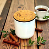 Candle burning on a wooden surface with cinnamon sticks and a glass of liquid in the background