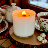 Candle in a glass holder on a wooden surface with tea cups and decorative items in the background.